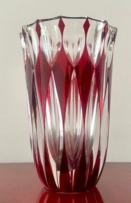 un vase rouge posé sur une table, avec un mur blanc en arrière-plan