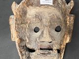an old wooden mask on a black surface with a tag on it