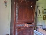 une grande armoire en bois dans une pièce où sont accrochés des tableaux au mur