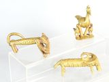 three gold figurines of animals on a clear stand