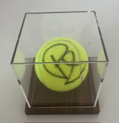 une balle de tennis jaune dans une boîte transparente posée sur une table