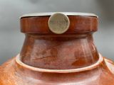 a brown vase with a metal lid on a table