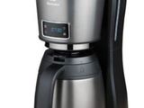 La cafetière est posée sur une surface blanche recouverte d'un couvercle noir.