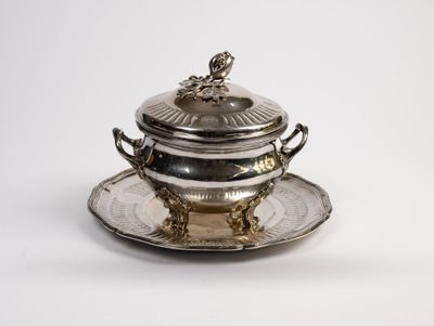 an antique silver plate with a lid and a saucer on a saucer