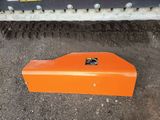 an orange plow blade laying on the ground in front of a machine