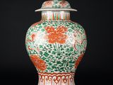 un vase orange et vert muni d'un couvercle, posé sur une surface noire