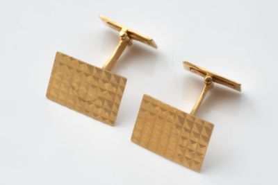 deux boutons de manchette en or posés sur une surface blanche, sur fond blanc
