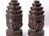pair of carved wooden buddha heads on pedestals on a white background