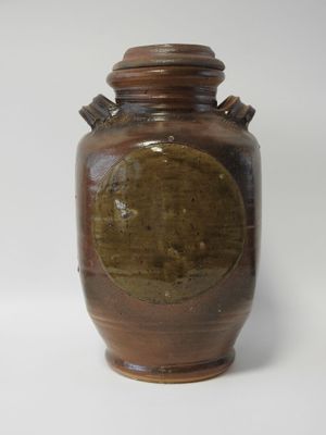 un vase marron avec un couvercle marron posé sur une surface blanche