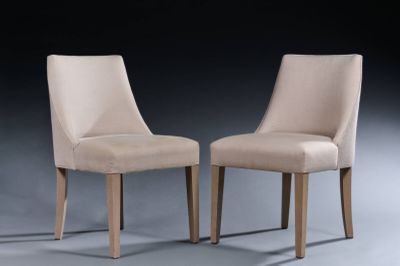 pair of beige upholstered chairs against a black background