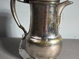 une cafetière ancienne en argent avec son couvercle, posée sur une table