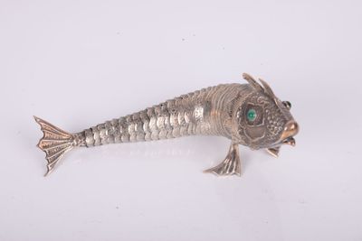 silver fish broochle with green eyes on a white surface