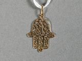 un pendentif en forme de main de Hamsa dorée, muni d'un cordon blanc, sur fond gris
