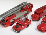 Plusieurs camions de pompiers miniatures sont alignés sur une surface blanche