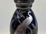 a black vase with a bird on it on a table