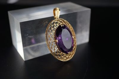 une photo d'un pendentif en pierre violette posé sur une boîte transparente
