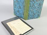 an open book with a blue and green cover next to a notepad