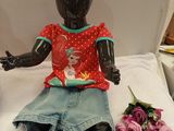 a doll sitting on a bed next to a flower