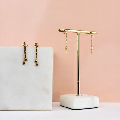 une paire de boucles d'oreilles en or posées sur un socle en marbre, près d'un mur rose