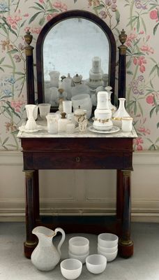une table sur laquelle sont posés un miroir et des tasses, devant un mur recouvert de papier peint