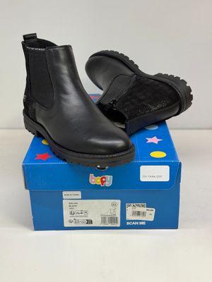 des bottines en cuir noir posées sur une boîte bleue, elle-même posée sur une surface blanche