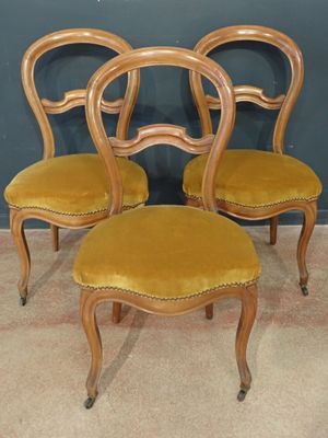 four chairs with yellow velvet upholstered seats in front of a blue wall