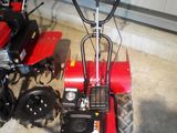 un petit tracteur rouge garé à côté d'une petite tondeuse rouge