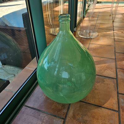 un grand vase vert posé sur un sol carrelé près d'une fenêtre
