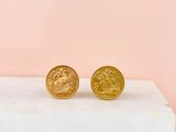 a pair of gold coin stud earrings sitting on top of a marble block