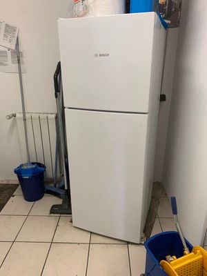 un réfrigérateur blanc dans un coin de la pièce, à côté d'une serpillière et de seaux
