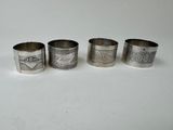 four silver napkin rings with designs on them on a white surface