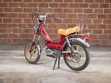 a small red motorcycle parked in front of a brick wall