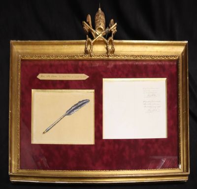 tableau dans un cadre doré représentant un stylo et un encrier sur fond noir