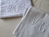 two white towels with embroidered monograms on them on a bed