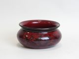 a red bowl with a black rim sitting on a white surface