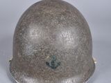 Un vieux casque repose sur une surface blanche, avec un fond gris.
