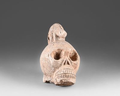 un gros plan sur une figurine en argile représentant un crâne avec un oiseau perché sur la tête