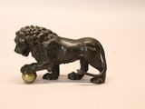 une statue en bronze représentant un lion tenant une balle entre ses pattes