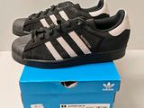 une paire de baskets Adidas noires et blanches dans une boîte bleue