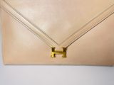 a beige leather clutch bag with a gold h logo on the front