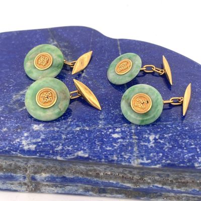 trois paires de boutons de manchette verts et dorés posés sur une dalle de pierre bleue