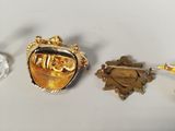 two gold colored brooches and a glass of wine sit on a table