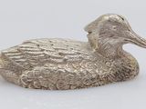 a silver duck figurine sitting on top of a white surface