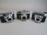 three old cameras sitting side by side on a white surface