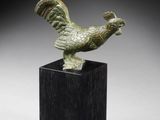 une figurine en bronze représentant un coq, posée sur un socle noir