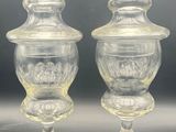 two clear glass vases with lids on a black surface