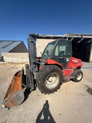 a red tractor parked in front of a building with a snow plow