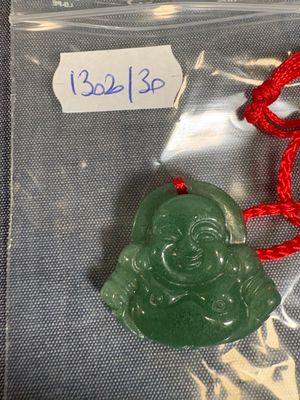 un pendentif représentant un Bouddha en jade vert, suspendu à un cordon rouge