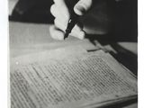 photographie en noir et blanc d'une personne en train d'écrire sur une feuille de papier