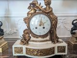 une horloge en or posée sur une table en marbre, flanquée de deux lampes